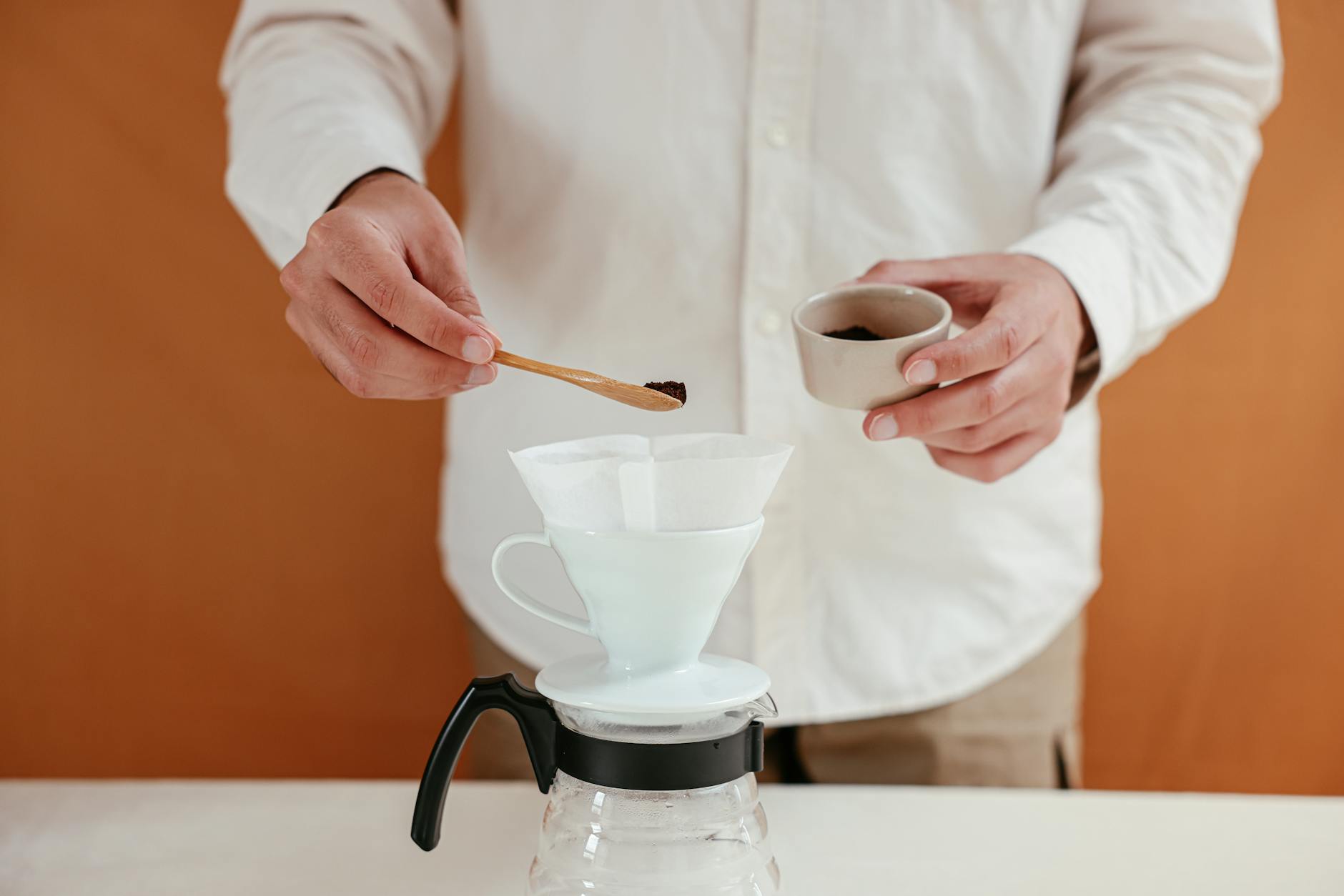 Close-up of a man using a dripper and filter to prepare pour over coffee.