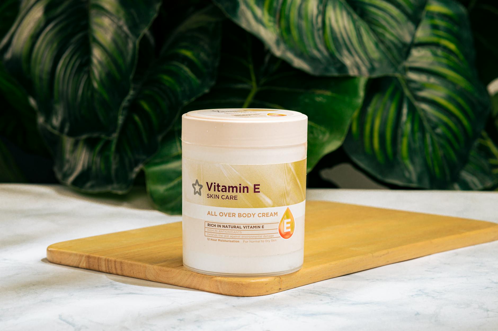 Vitamin E skin care cream on a wooden tray with green foliage background.
