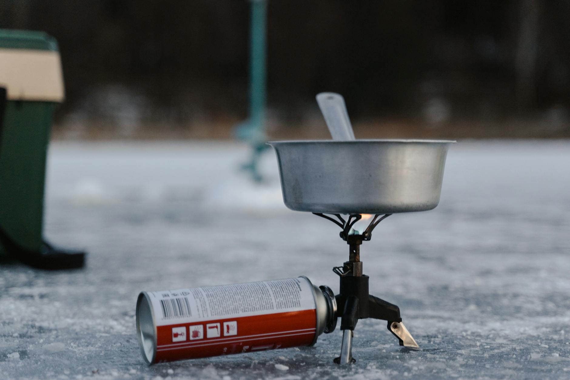 A camping stove setup on ice including a pot and butane canister for winter outdoor cooking.